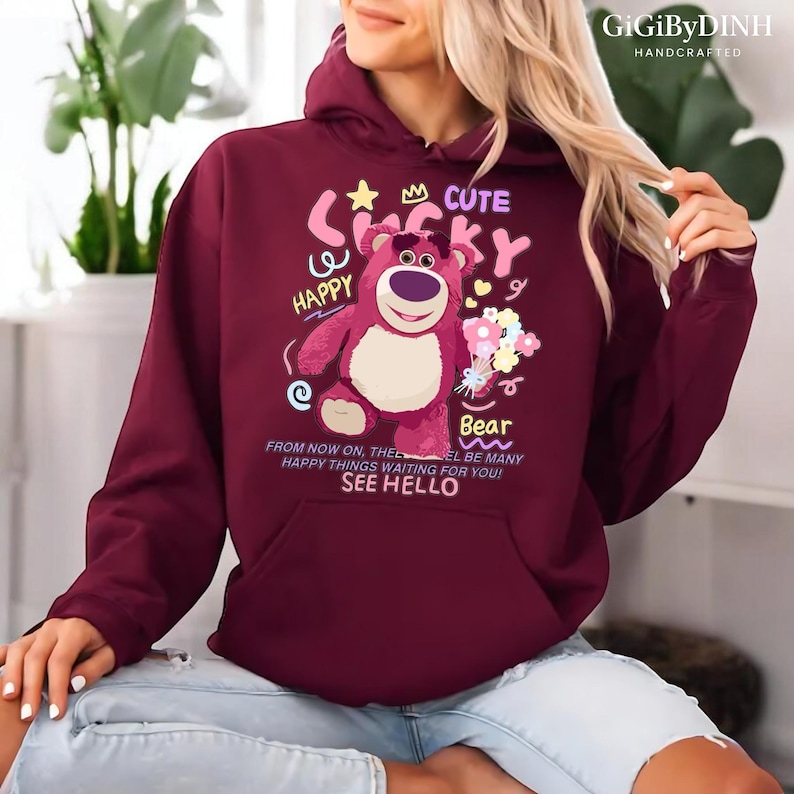 A woman wearing a burgundy hoodie with a cartoon bear design and text on it.