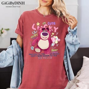 A woman wearing a red t-shirt with a cartoon bear and text printed on it.