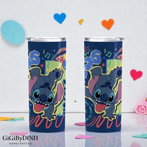two tall, cylindrical tumblers with a colorful, cartoonish design of a character on them. The character appears to be a character from the Disney movie Lilo & Stitch. The tumblers are placed on a white surface, surrounded by confetti and heart-shaped decorations.