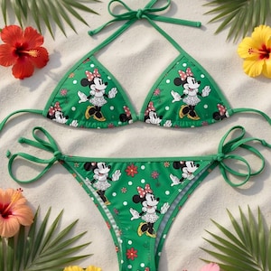 May include: Green bikini set featuring a Minnie Mouse print with white polka dots and red flower accents. The top and bottom are tied with green strings. The image includes the text "GiGiByDinh HANDCRAFTED".