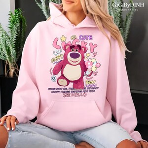 A woman wearing a pink hoodie with a cartoon character and text printed on it.