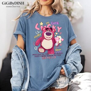 A woman wearing a blue t-shirt with a cartoon bear graphic and text, along with a denim jacket.