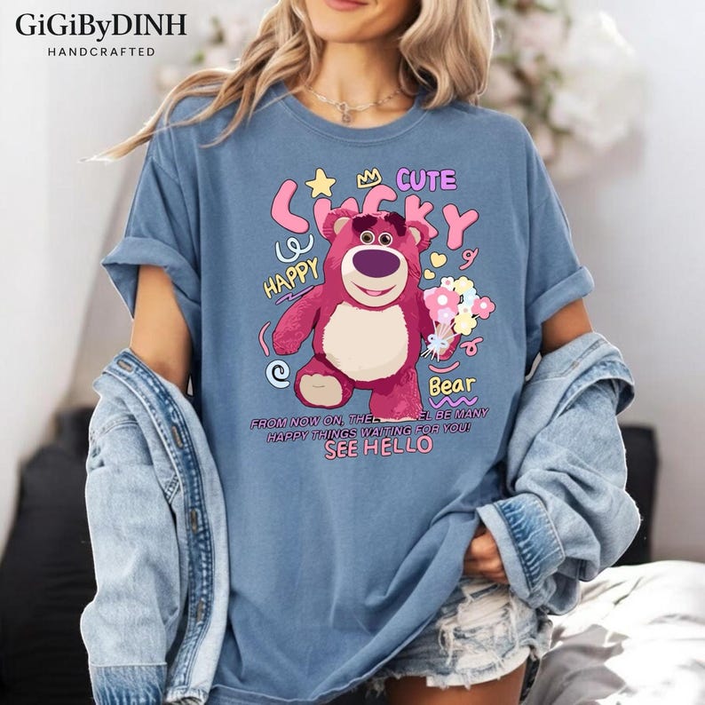 A woman wearing a blue t-shirt with a cartoon bear graphic and text, along with a denim jacket.