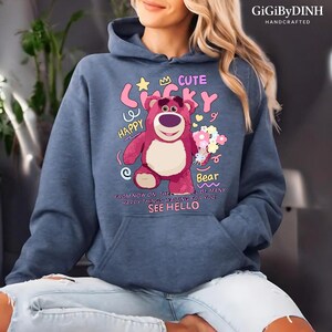 A woman wearing a blue hoodie with a cartoon bear design and text printed on it.
