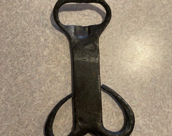 May include: A black metal bottle opener with a unique design. The opener has a loop on the top for opening bottles and two loops on the bottom for hanging.
