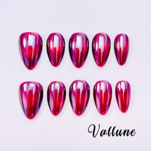 Puede incluir: Un conjunto de diez uñas artificiales brillantes en forma de lágrima, en un tono rojo-púrpura vibrante. Las uñas tienen un acabado metálico reflectante. La palabra "Vallune" está escrita en cursiva en la parte inferior.