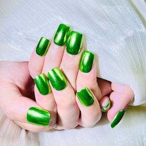 May include: Fingernails painted with a vibrant, reflective metallic green polish. The finish is smooth and glossy, creating a mirror-like effect that catches the light across the surface of each nail, showcasing a bright, saturated emerald hue.