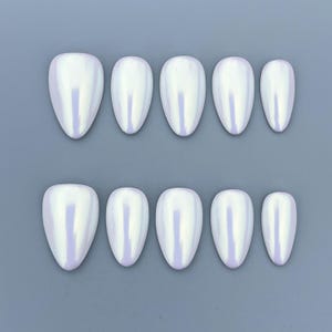 May include: A set of ten pearlescent, oval-shaped false nails arranged in two rows on a gray background. The nails have a glossy finish and reflect a subtle iridescent sheen of lavender and white.
