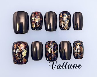May include: A set of ten press-on nails featuring a mix of solid metallic bronze and dark brown nails with embedded gold and copper foil flakes. The text Vallune is printed in black script at the bottom right of the nail set arrangement.