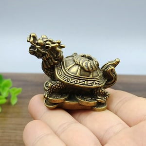 Pode incluir: Uma figura de latão detalhada de uma criatura mítica, uma tartaruga dragão. A escultura apresenta detalhes intrincados na concha, cabeça e pernas. A tartaruga dragão é um símbolo de longevidade e prosperidade.