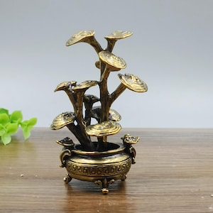 May include: A bronze-colored decorative sculpture of a stylized plant with multiple mushroom-shaped tops. The plant is in a detailed pot with a geometric pattern. The sculpture is on a wooden surface.