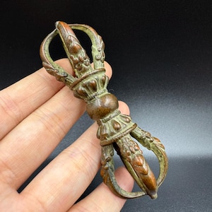 Könnte beinhalten: Ein bronzefarbener Vajra, ein Ritualobjekt mit einer zentralen Kugel und stilisierten Zacken. Das Objekt weist komplizierte Details und ein verwittertes Aussehen auf, was auf sein Alter hindeutet. Das Design weist florale und geometrische Muster auf.