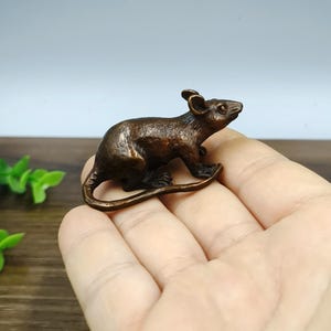 May include: A bronze-colored rat figurine. The rat is sculpted in a realistic pose, with its tail curled and its ears perked up. The figurine is small, detailed, and has a polished finish. It is a decorative item.