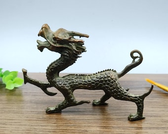 May include: A bronze-colored dragon figurine with intricate details. The dragon has a detailed head, a serpentine body, and is posed in a dynamic stance. The figurine is on a wooden surface.