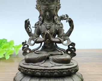 May include: Bronze-coloured statue of a seated deity with multiple arms, adorned with a crown and intricate jewellery. The figure is in a meditative pose, hands clasped in prayer, seated on a lotus flower base. A detailed religious sculpture.