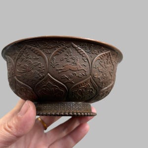 Op de afbeelding: Een bronzen kom met ingewikkelde reliëfsnijwerk. De kom heeft een gedetailleerd patroon van bloemen- en diermotieven, waaronder een springende haas. De kom heeft een decoratieve basis en een brede rand.