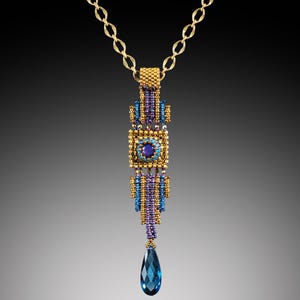 May include: A gold-toned necklace with a beaded pendant. The pendant features a central square with a blue gemstone, surrounded by blue, purple, and gold beads. A large, teardrop-shaped blue gemstone hangs from the bottom.