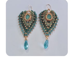 May include: A pair of handcrafted leaf-shaped earrings. The earrings feature a combination of teal, gold, and green beads, with a teardrop-shaped blue gemstone dangling from the bottom. The earrings have gold-colored ear wires.