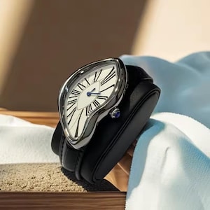 May include: A unique wristwatch with a distorted, melting-style silver case and a white face with black Roman numerals. The watch has blue hands and a black leather strap. A small blue gem is set into the side of the watch.