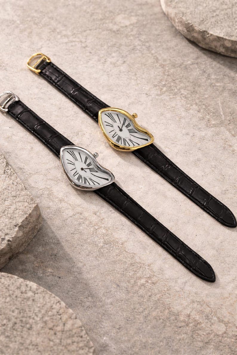 May include: Two unique wristwatches with a melting clock face design. One watch has a silver case, the other is gold-toned. Both have black leather straps and white clock faces with black Roman numerals.