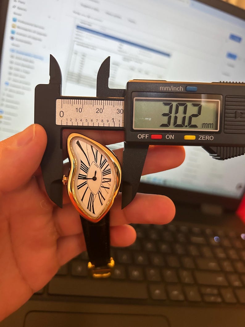 May include: A gold-toned wristwatch with a white face and black Roman numerals. The watch has a unique, curved shape and a black leather band. The digital caliper shows a measurement of 30.2 mm.