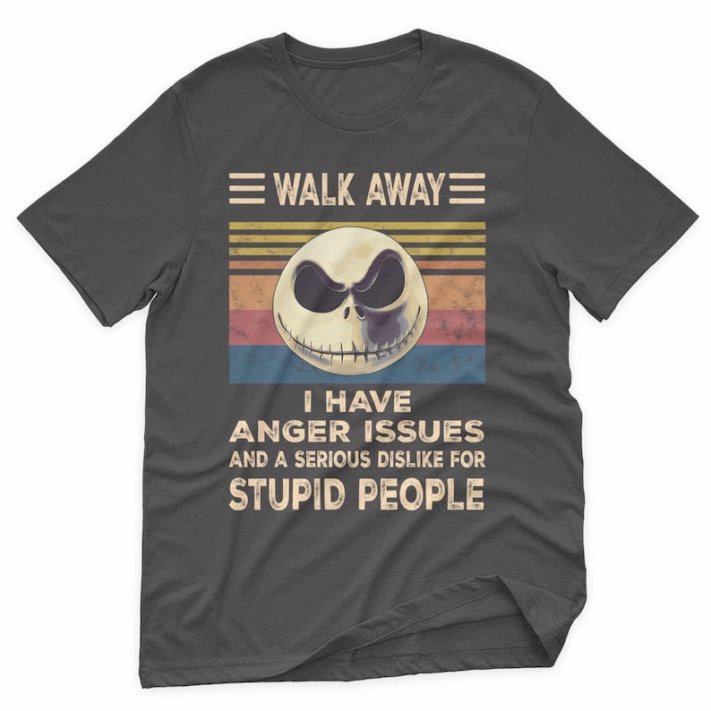 May include: Dark gray t-shirt featuring a graphic of a skull with the text "WALK AWAY" above and "I HAVE ANGER ISSUES AND A SERIOUS DISLIKE FOR STUPID PEOPLE" below. The skull has a sinister expression.