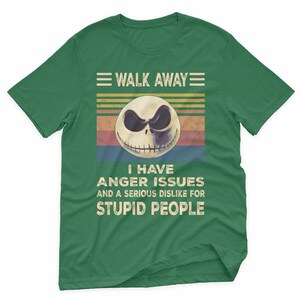 May include: Green t-shirt featuring a graphic of a skull with the text "WALK AWAY" above and "I HAVE ANGER ISSUES AND A SERIOUS DISLIKE FOR STUPID PEOPLE" below. The skull has a black and white design.