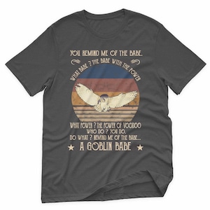 May include: Dark gray t-shirt with a graphic featuring an owl with outstretched wings inside a sunset design. Text includes "YOU REMIND ME OF THE BABE" and "A GOBLIN BABE."
