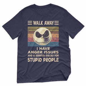 May include: Navy blue t-shirt with a graphic of a skull with a sinister expression. The text reads "WALK AWAY" above the skull and "I HAVE ANGER ISSUES AND A SERIOUS DISLIKE FOR STUPID PEOPLE" below.