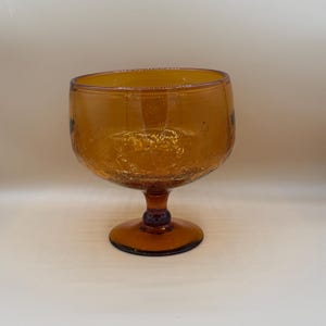 May include: Amber-colored, vintage-style glass goblet with a wide bowl and a short stem. The glass has a crackled texture, adding to its antique appearance. The goblet is designed for serving beverages.
