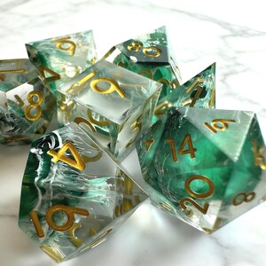May include: A set of seven polyhedral dice. The dice are clear with green and white marbling, and gold-colored numbers. The dice are designed for tabletop role-playing games.