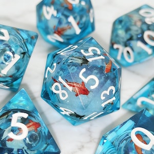 May include: A collection of polyhedral dice with a clear, blue resin design. Each die features a detailed image of koi fish in shades of red, black, and white. The numbers are white and easy to read, making them ideal for tabletop gaming.