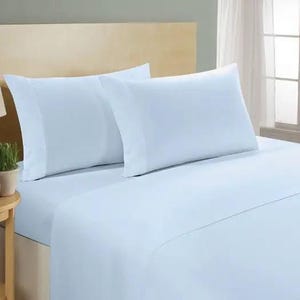 Puede incluir: Un juego de sábanas azul claro con dos fundas de almohada a juego. La ropa de cama está cuidadosamente colocada sobre una cama con un cabecero de color claro. Las sábanas y fundas de almohada son de tela suave y lisa.
