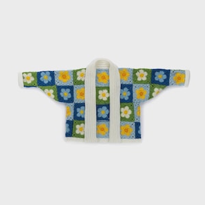 May include: A colorful, crocheted cardigan with a floral pattern. The cardigan features a patchwork design with blue, green, yellow, and white flower squares. A white, knitted collar and trim complete the look. The garment is displayed on a white background.