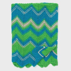 May include: A folded, knitted blanket with a chevron pattern in shades of teal, green, and light gray. The blanket has a scalloped edge and a folded corner, showcasing the pattern's design. The knitted texture is visible.