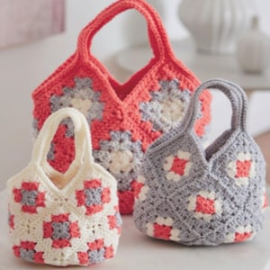 Puede incluir: Tres bolsos de crochet hechos a mano de diferentes tamaños. Los bolsos presentan un diseño de granny square con cuadrados de color coral, gris y crema. Cada bolso tiene un asa a juego. Los bolsos se exhiben sobre una superficie clara.