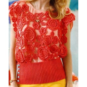 May include: A coral crochet top with a floral pattern. The top has a round neckline and short sleeves. The lower section is a solid coral colour with light blue buttons. The top is worn with yellow trousers.
