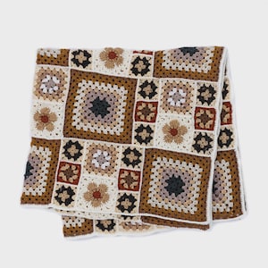 Pode incluir: Uma manta de crochê feita à mão com um design de patchwork. A manta apresenta padrões quadrados em tons de marrom, creme e preto. O design inclui padrões florais e geométricos. A manta está dobrada.
