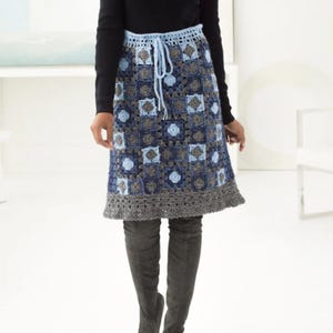May include: A blue, grey, and white crochet skirt with a drawstring waist. The skirt features a geometric pattern of squares and floral shapes. The hem is a solid grey colour.