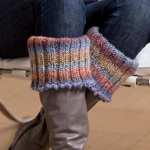 May include: A pair of colorful knitted leg warmers in shades of orange, blue, and yellow. The leg warmers are worn over brown leather boots and under blue jeans. The knitted design features a ribbed pattern with a scalloped edge.