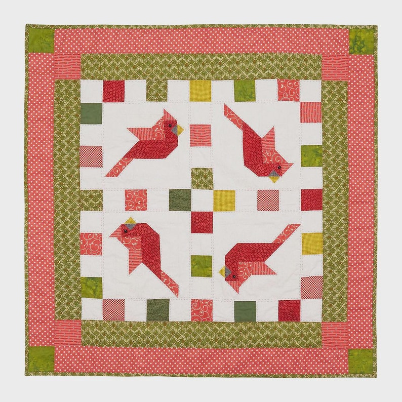 K&ouml;nnte beinhalten: Ein quadratischer Quilt mit vier roten Kardinalvogel-Designs auf wei&szlig;em Hintergrund. Der Quilt hat einen roten und gr&uuml;nen Rand mit einem Tupfenmuster. Die V&ouml;gel sind aus rotem Stoff mit gelben Schn&auml;beln.