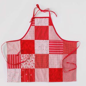 May include: A patchwork apron in various shades of red, featuring a mix of patterns including polka dots, hearts, stripes, and gingham. The apron has a red trim, neck strap, and waist ties. The apron is designed for kitchen use.