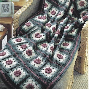 May include: A handmade crochet blanket draped over a wicker chair. The blanket features a repeating pattern of square blocks with white, dark teal, and burgundy floral designs. The blanket's edges are finished with a dark teal border.