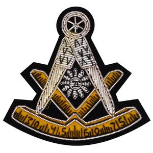 May include: A black embroidered patch featuring a Masonic symbol. The design includes a compass, square, and ruler in gold and silver thread. The patch has a black border and a sun-like emblem in the center.