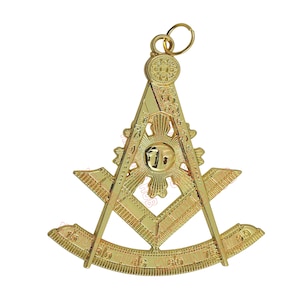 May include: A gold-colored pendant featuring a Masonic symbol. The pendant includes a compass, a square, and a sunburst design. The pendant has a ring at the top for attachment.