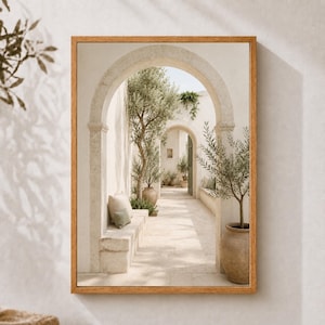 May include: A framed wall art print depicting a sunlit Mediterranean courtyard with stone arches, a built-in stone bench with cushions, and potted olive trees. The scene features light beige stone walls, a paved walkway, and soft shadows.