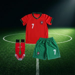 Puede incluir: Un uniforme de f&uacute;tbol rojo con el n&uacute;mero 7, pantalones cortos verdes y calcetines rojos. La camiseta y los pantalones cortos presentan el emblema de la selecci&oacute;n portuguesa. La camiseta tiene cuello y ribetes verdes. Los calcetines tienen las letras "FPF".