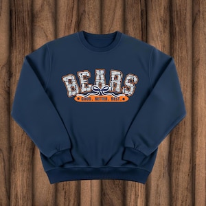 May include: Navy blue sweatshirt with the word "BEARS" in a stylized design across the chest. The text is white and orange, with a pattern. Below the word "BEARS" is the phrase "GOOD. BETTER. BEST." in orange.