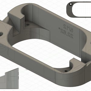 Puede incluir: Un objeto rectangular gris renderizado en 3D con esquinas redondeadas, que presenta una abertura central y varios agujeros circulares. El objeto tiene una pieza más pequeña y a juego, y el texto "SH2 SS" es visible en el lateral. El diseño sugiere un componente mecánico o industrial.