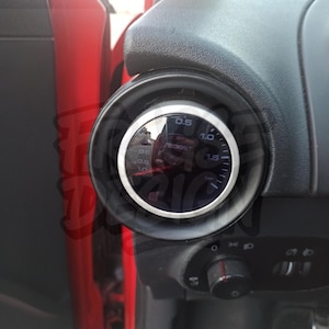 Può includere: Un manometro di sovralimentazione nero e argento installato nel cruscotto di un'auto. L'indicatore ha un quadrante circolare con segni bianchi e un ago che indica i livelli di pressione. L'indicatore è inserito in una cornice nera.